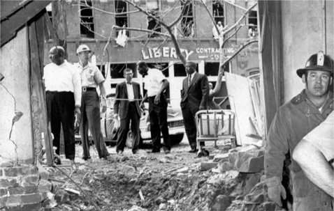 In this Sept. 15, 1963 file photo, emergency workers and others stand around a large crater from a bomb which killed four black girls in the Sixteenth Street Baptist Church in Birmingham, Ala. The windows of the building across the street in the background were also blown out. (AP Photo)